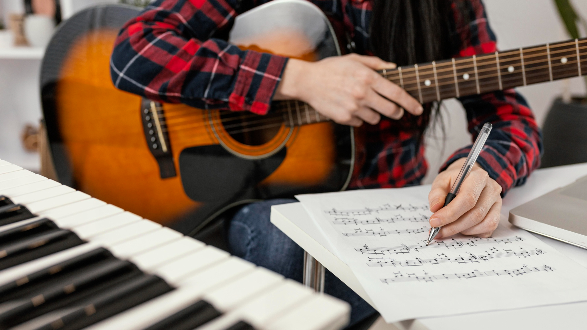 Tronco de um homem segurando um violão e fazendo uma anotação em uma partitura
